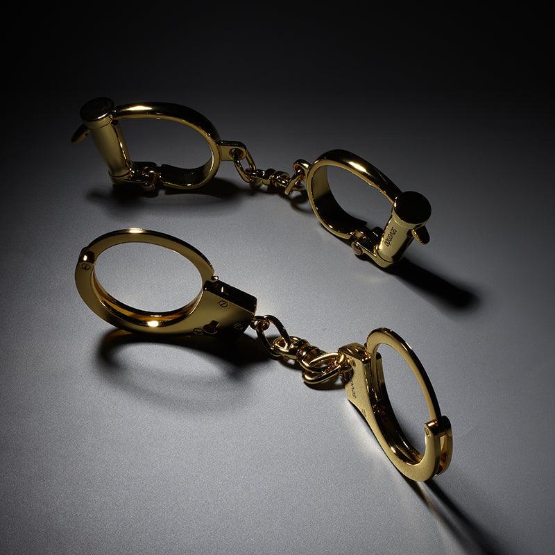 Two SEVANDA gold handcuffs sets side by side, showing the horseshoe shaped bow and the chain