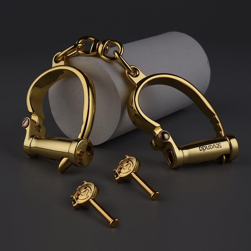 SEVANDA gold handcuffs resting on a grey roll with the two gold keys in front